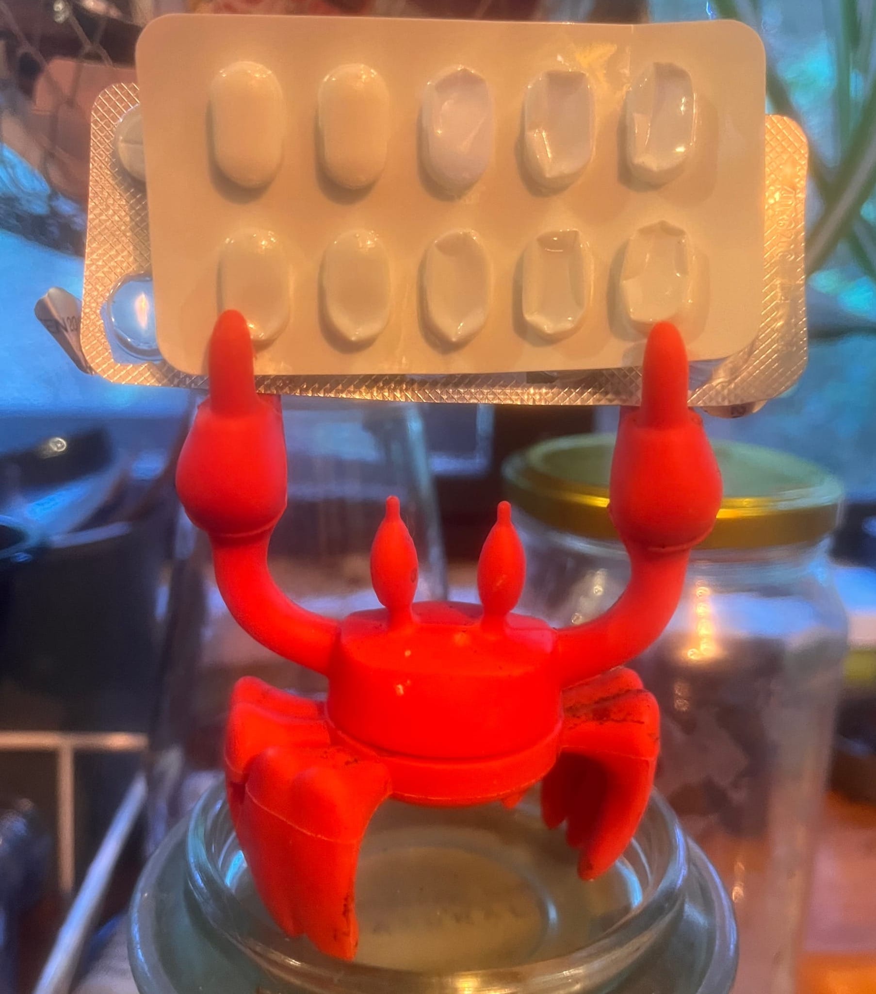 silicone crab with raised pincers holding up two sheets of pills